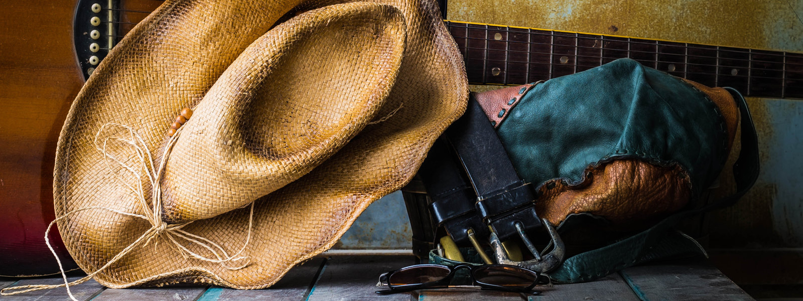 Cowboy hat, guitar, boots and sunglasses on a rustic tabletop